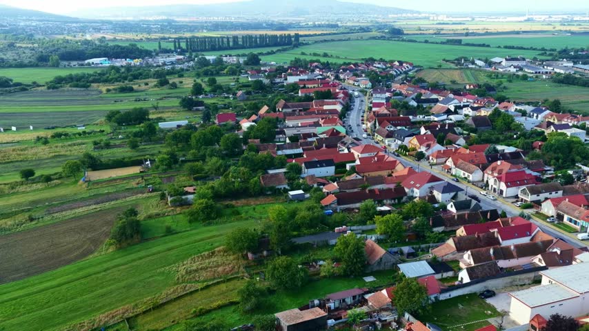 Aerial view of Stupava in Slovakia following a residential street lined with red roof houses beside gardens and cultivated fields on the town outskirts
