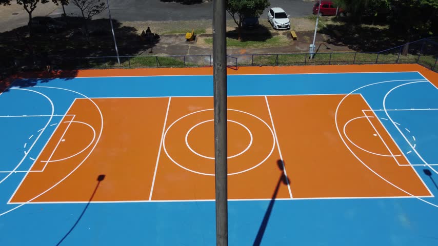 Cinematic aerial reveal, Brightly colored outdoor sports court in Brasilia, Brazil, recreational facilities surrounded by trees and open public spaces