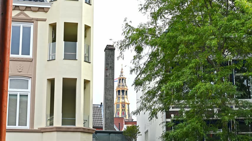 A view of the historic Der Aa-kerk tower framed by modern residential buildings and trees in Groningen, Netherlands.