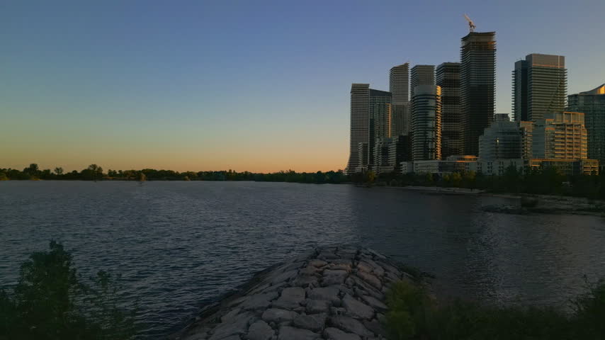 Static shot of Humber Bay condo skyscrapers and rock breakwater on Lake Ontario at golden hour, Toronto.
