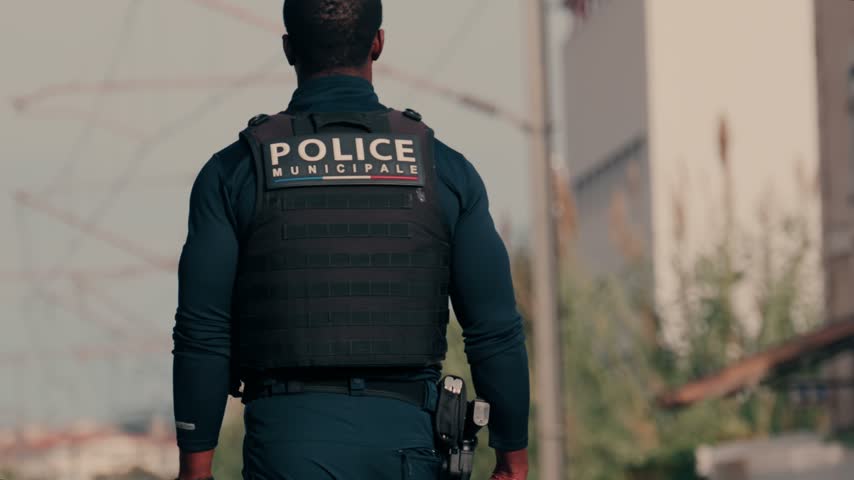 African American officer in police municipale uniform patrolling outdoors. Focus on back tactical gear and holster.