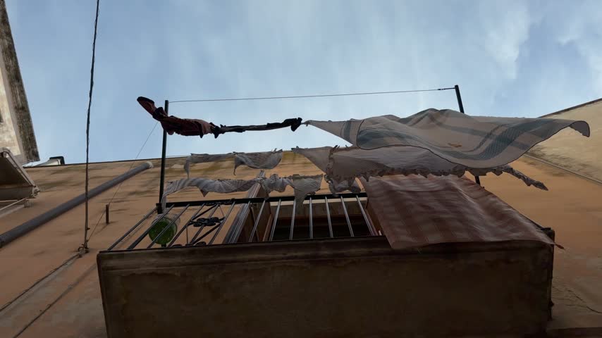 Clothesline with a white sheet, a checked cloth and a red garment blowing in the wind on a rooftop in Bari old town, Puglia, Italy, under a blue sky