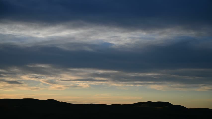 Time lapse of late day sunset clouds moving above rolling prairie hills
