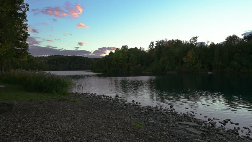 Calm lake water reflects colorful evening clouds beside a wooded shoreline at Green Lakes State Park, New York.