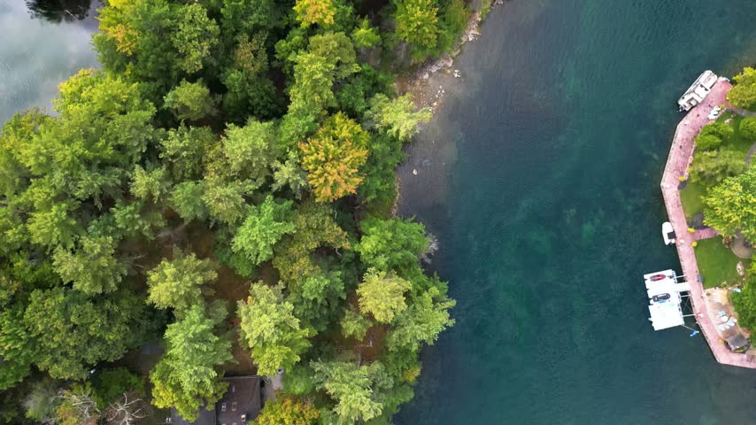 Top down aerial view of an island shoreline with colorful autumn trees beside clear blue green water.