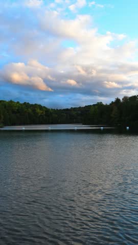 A horizontal lakeside composition shows reflective water, shoreline trees and warm clouds at Green Lakes State Park, New York.