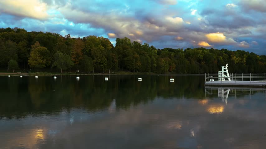 Colorful evening clouds appear above and within calm lake reflections beside a wooded beach at Green Lakes State Park, New York.