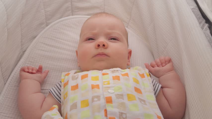 Adorable infant baby boy lies in white crib, smiling and laughing happily in morning light