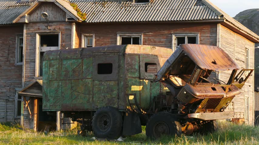 The remains of an old dilapidated car next to an equally ancient dilapidated house in an abandoned village.