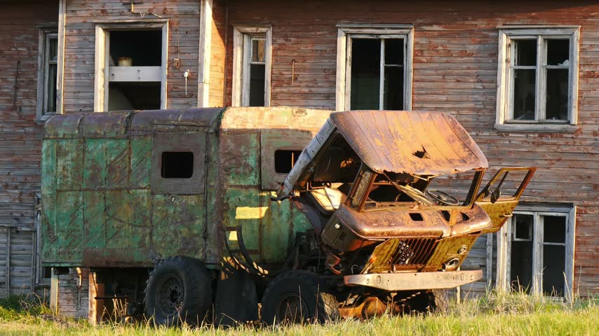 The remains of an old dilapidated car next to an equally ancient dilapidated house in an abandoned village.