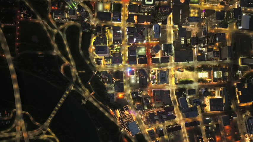 Top down drone flight over downtown Edmonton at night, revealing illuminated blocks, intersections, moving traffic and a geometric street grid during the early commute.