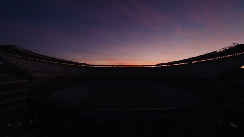 Empty American Football Stadium at Dusk with Bright Floodlights Illuminating the Green Turf Field and Rolling Mist Across the Seating Bowl during Twilight Hours