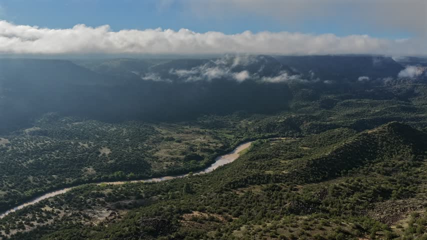 Aerial view of the lush Rio Grande Valley with low hanging clouds and fog drifting over the landscape in White Rock, New Mexico, United States.