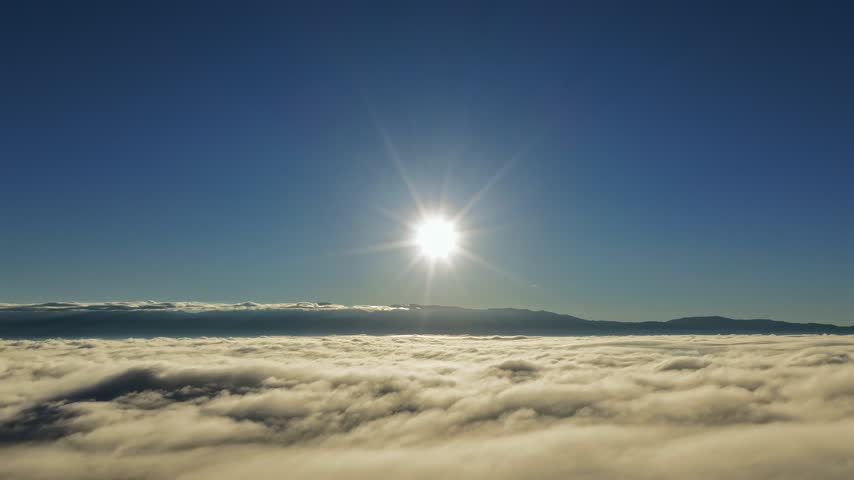 Aerial view of sun shining over a dense sea of fog clouds above the landscape in White Rock, New Mexico, United States.