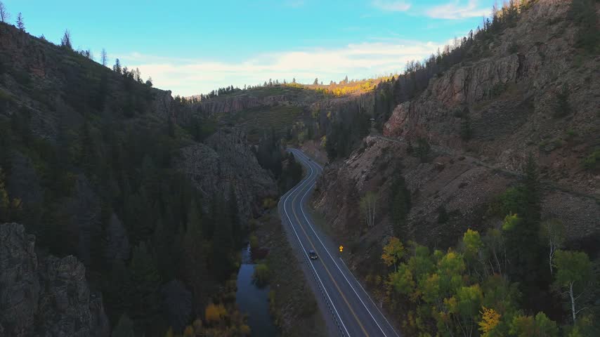 Aerial view of a winding road through Black Canyon of the Gunnison National Park with steep rocky cliffs, pine trees, and a river in Gunnison, Colorado, United States.