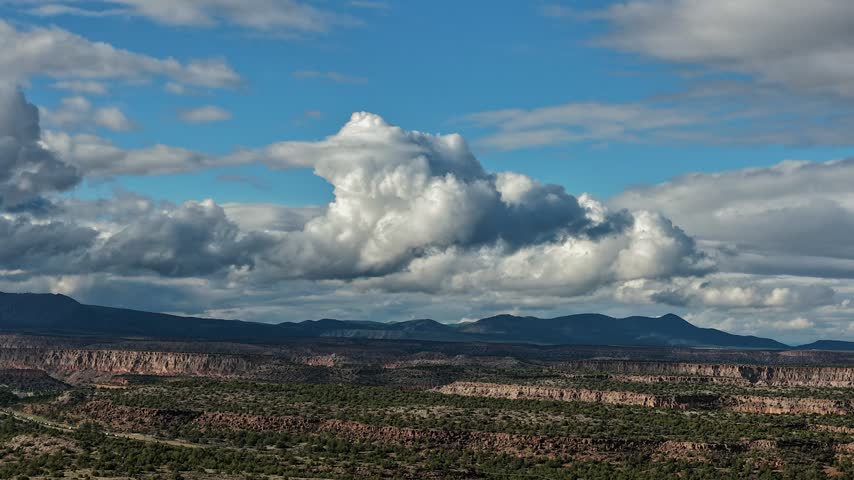 Aerial view of dramatic cloud formations moving over a vast mesa landscape with sparse vegetation in White Rock, New Mexico, United States.