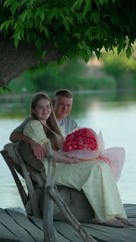 A smiling young couple sits by the river. Romantic date concept.