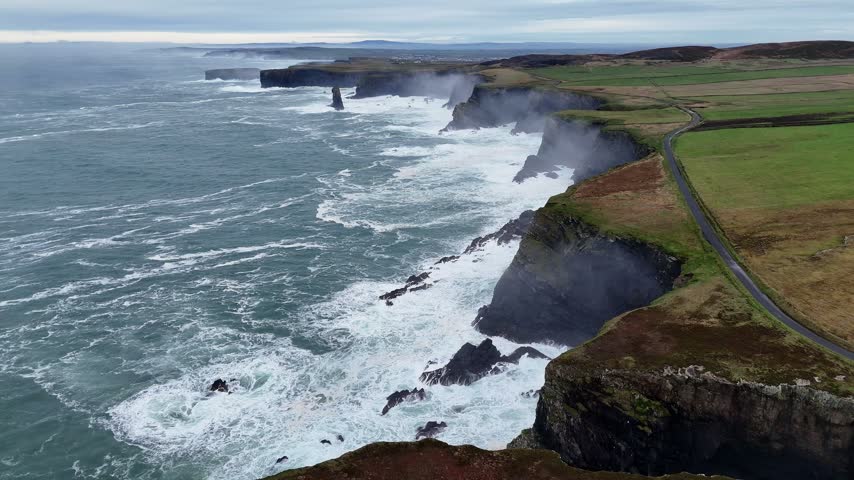 Aerial view of a narrow road following the grassy edge of the Atlantic cliffs at Downpatrick Head, County Mayo, with waves breaking along the rocky coast.