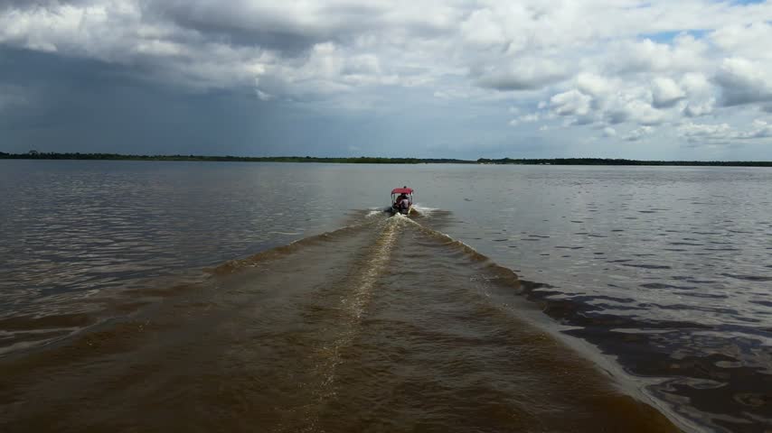 Aerial view of a small motorboat leaving a wake on the Amazon River under a cloudy sky in Manaus, Amazonas, Brazil.