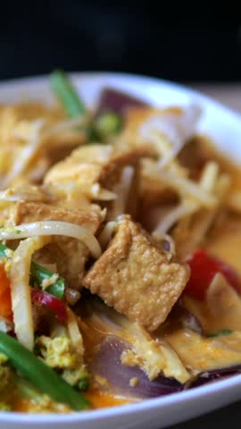 Tofu noodle stir fry is served with crisp bean sprouts, tomato, greens and egg. Close food presentation highlights browned tofu and colorful ingredients in satisfying savory dish, with noodles