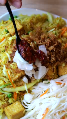 Spoon adds glossy chili sauce to colorful noodle salad arranged with tofu, shredded vegetables and white dressing. Finished dish highlights fresh ingredients and appetizing food styling.