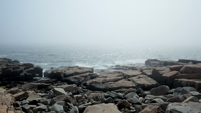 Crashing ocean waves along the rugged pink granite rock ledges enveloped in thick fog at Schoodic Point in Acadia National Park, Maine.