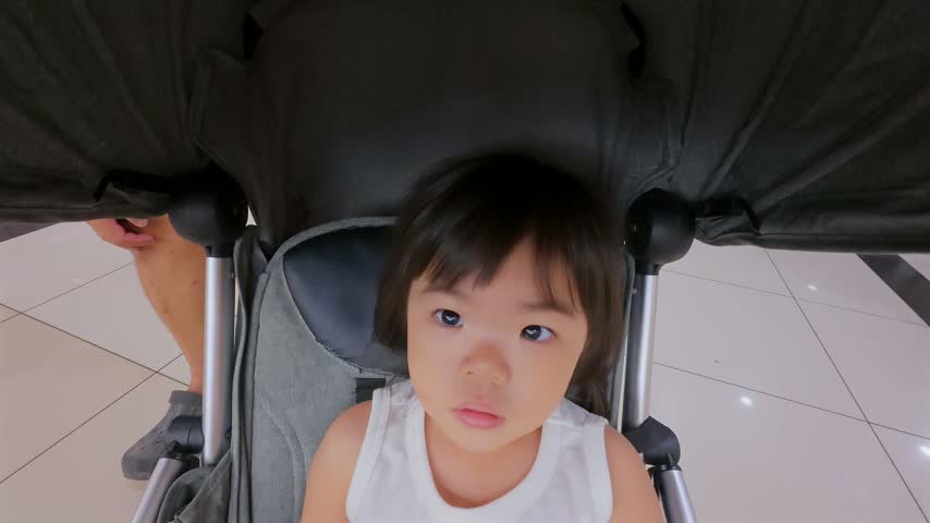 Close-up of child in white sleeveless top seated under stroller canopy.