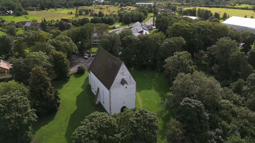 Aerial view of a historic white stone church surrounded by lush green trees and fields in Saare County, Estonia.
