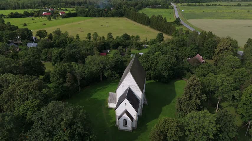 Aerial view of white church surrounded by lush green trees and fields in Saare County, Estonia.