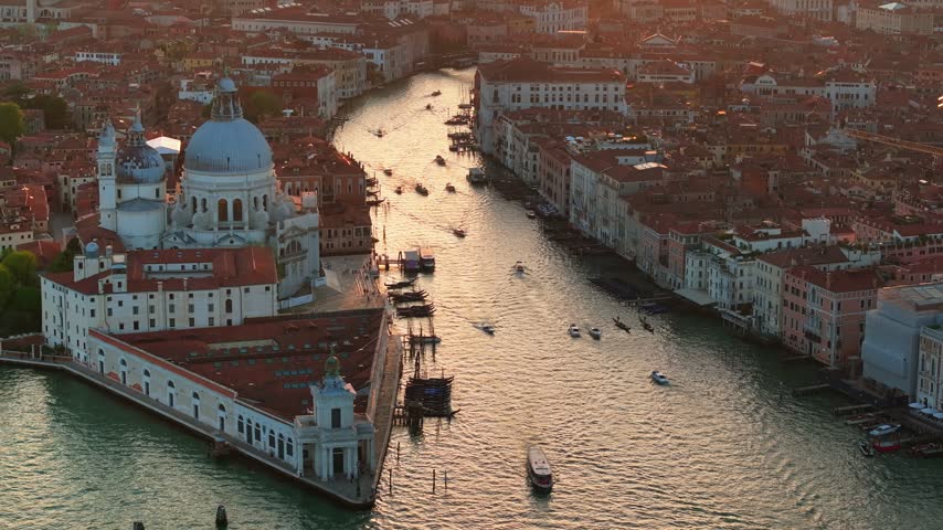 Stunning sunset drone shot of historic Basilica di Santa Maria della Salute and busy boat traffic on Grand Canal.
