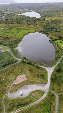 Aerial view of Bonny Glen Woods and lake with a camper van parked on a winding road in Portnoo, County Donegal, Ireland.
