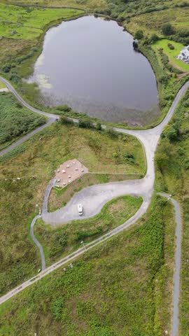 Aerial view of a lake surrounded by lush green landscape, winding paths, and a small parking area with a campervan near Bonny Glen Woods in Portnoo, County Donegal, Ireland.