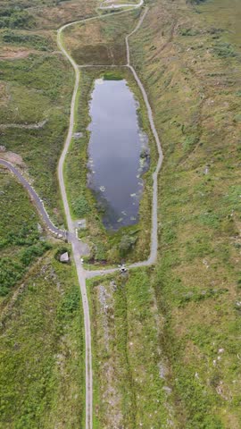 Aerial view of a small pond surrounded by lush green hills and walking paths in Bonny Glen Woods in Portnoo, County Donegal, Ireland.