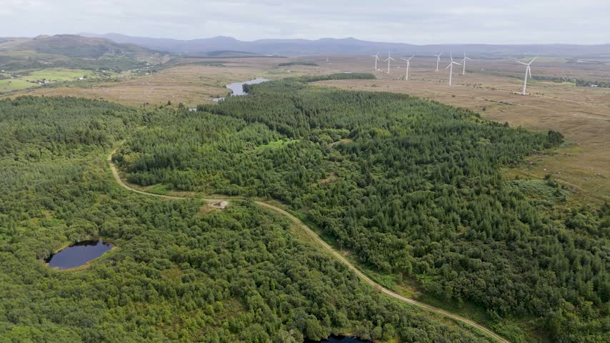 Aerial view of Bonny Glen Woods with wind turbines and a small pond in the surrounding landscape of Portnoo, County Donegal, Ireland.
