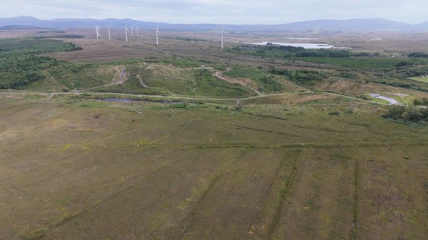 Aerial view of Bonny Glen Woods featuring wind turbines, rolling green fields, and a small pond under a cloudy sky in Portnoo, County Donegal, Ireland.