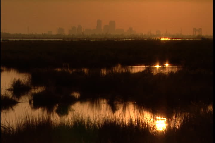 Orange sun reflecting on flooded marsh land, city skyline seen through orange haze in background in New Orleans after Hurricane Katrina (October 2005).