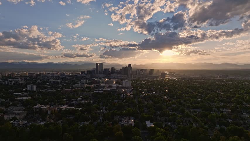 Aerial view of Denver skyline at sunset with dramatic clouds and distant mountains in Denver, Colorado, United States.