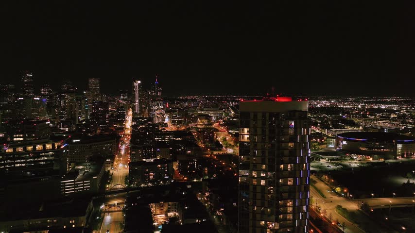 Aerial view of the illuminated Denver city skyline at night with glowing skyscrapers and urban street lights in Denver, Colorado, United States.