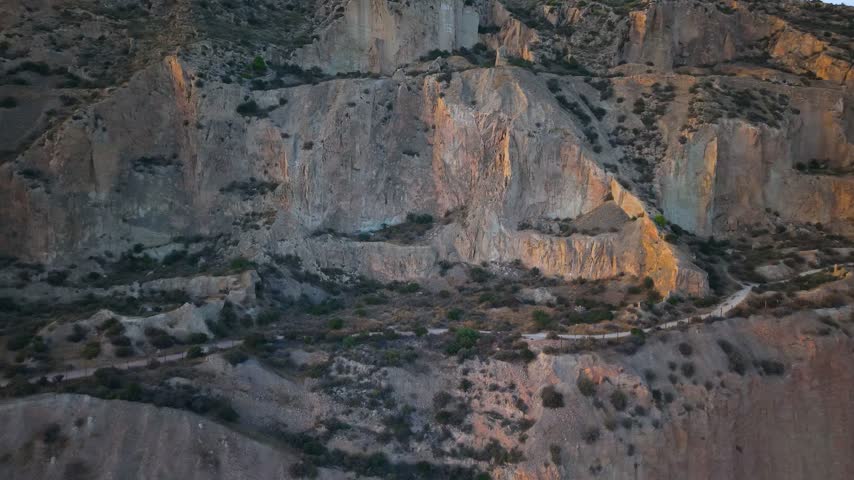 Aerial view of the rugged rocky cliffs and winding trails of the Alicante landscape during golden hour in Alicante, Valencian Community, Spain.
