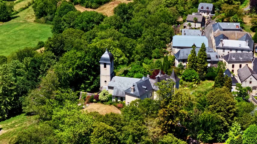Aerial view of the village of Beost featuring a historic stone church surrounded by lush green trees and traditional houses in the Pyrenees mountains, Beost, Nouvelle-Aquitaine, France.