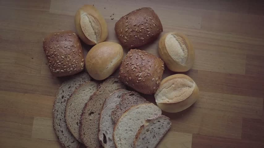 Top view shot of fresh whole grain bread slices and artisan rolls placed on wooden surface.