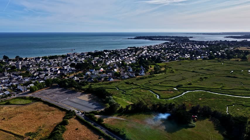 Aerial view of coastal town with houses, green fields, and blue sea in Nantes, Pays de la Loire, France.