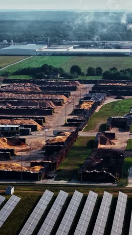 Aerial view of industrial wood storage facility with large piles of wood chips and solar panels in Suwalki, Podlaskie Voivodeship, Poland.