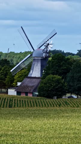 Aerial view of a traditional wooden windmill standing in a green field surrounded by trees under a cloudy sky in Konin, Wielkopolskie, Poland.