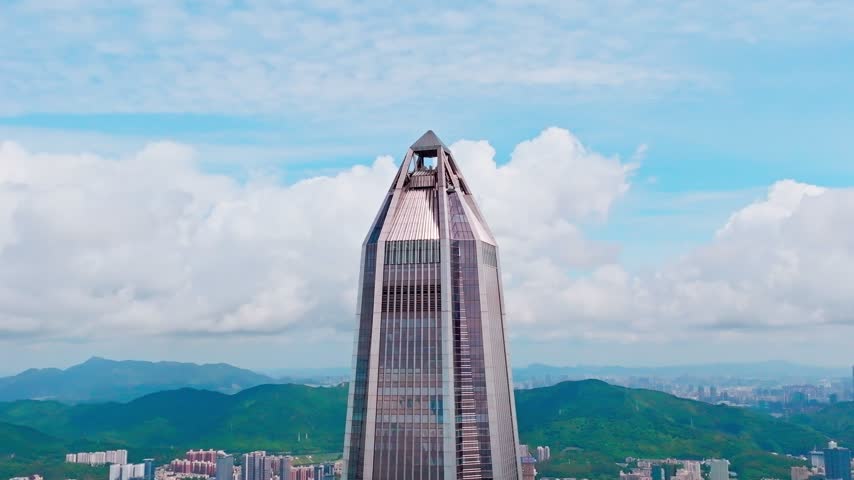 Elevated view of angular tower summit with distant green hills in Shenzhen, Guangdong, China. The scene features Ping An Finance Centre. Relevant to architecture and urban planning.