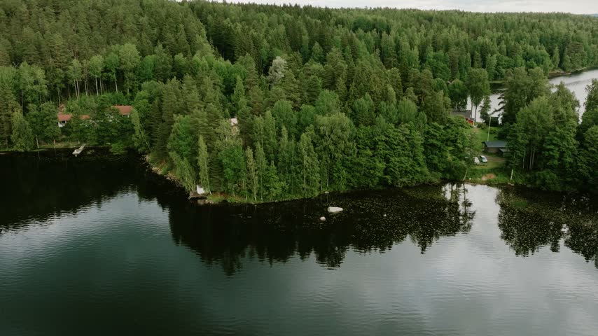 Aerial view of a serene lake surrounded by dense pine forests and small cabins in Hameenlinna, Kanta-Hame, Finland.