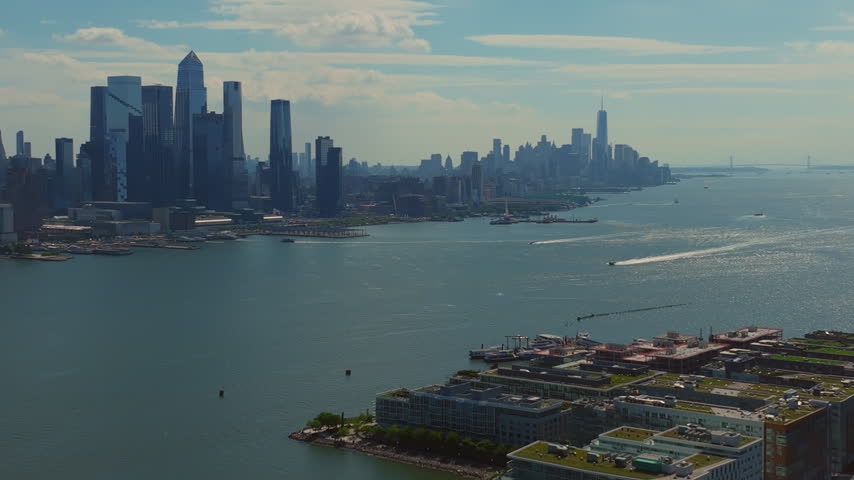 Elevated aerial view of the Hudson River and Manhattan skyline from Weehawken, New Jersey, with waterfront buildings and boat traffic below.