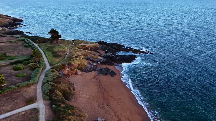 Aerial view of the rugged coastline with a sandy beach, rocky cliffs, and a winding path along the Atlantic shore in Nantes, Pays de la Loire, France.
