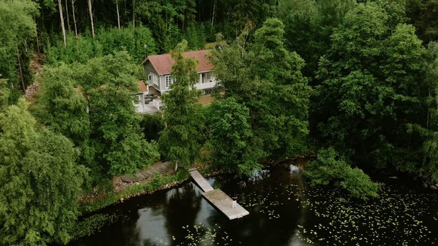 Aerial view of a house by a lake with a wooden pier surrounded by dense forest in Hameenlinna, Kanta-Hame, Finland.