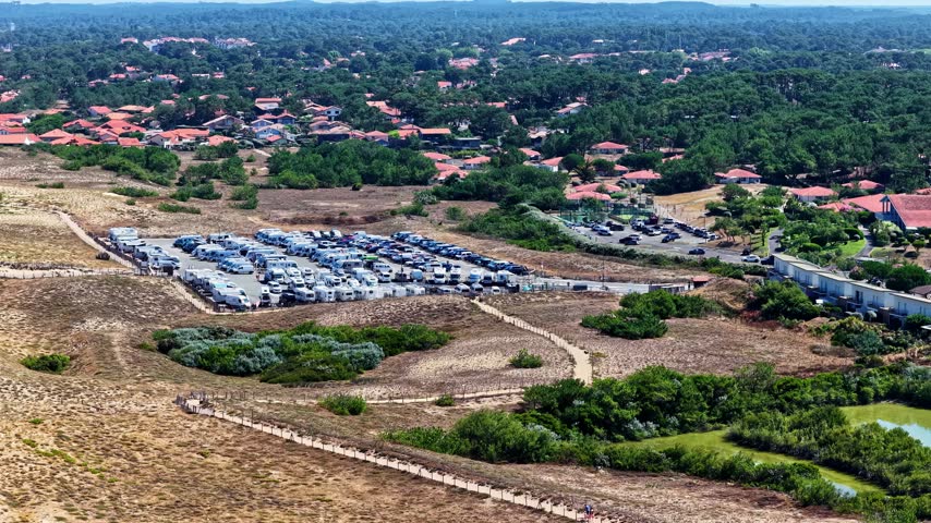 Aerial view of a large parking lot filled with numerous camper vans and recreational vehicles situated near a dense forest and coastal landscape in France.